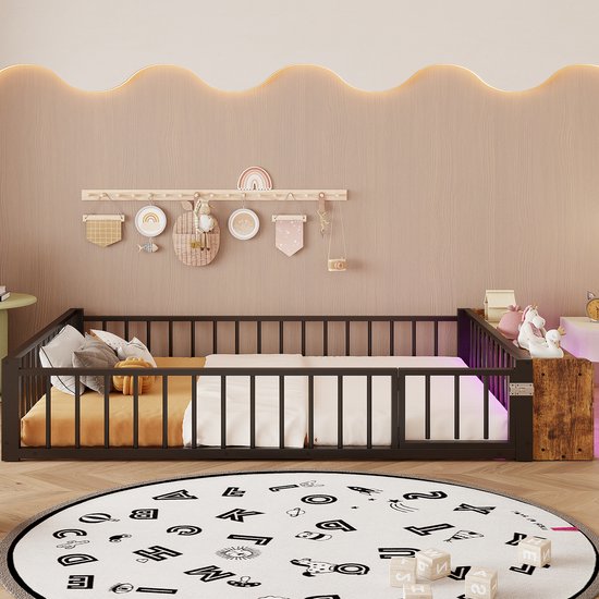 Kinderbed met zwart metalen spijlenhek en houten hoofdeinde met opbergvakken, opgemaakt met beddengoed in een kinderkamer.