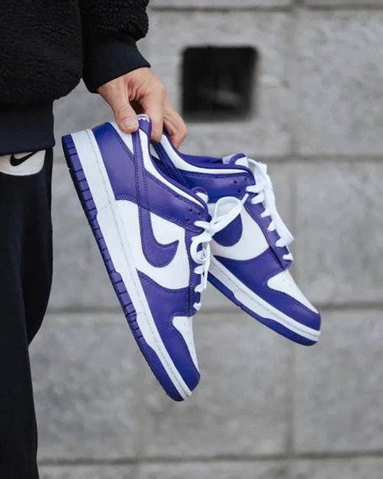 Paarse en witte Nike Dunk Low Retro sneakers, vastgehouden door een persoon.