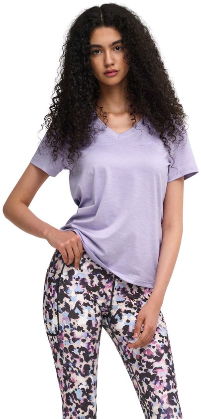Model in paars sportshirt met V-hals en een veelkleurige legging met abstracte print. Ze houdt haar shirt op.