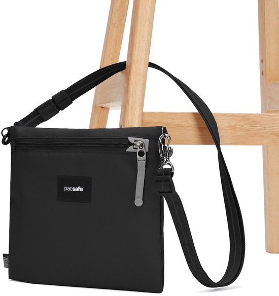 Zwarte Pacsafe crossbody tas, gedrapeerd over een stoel.