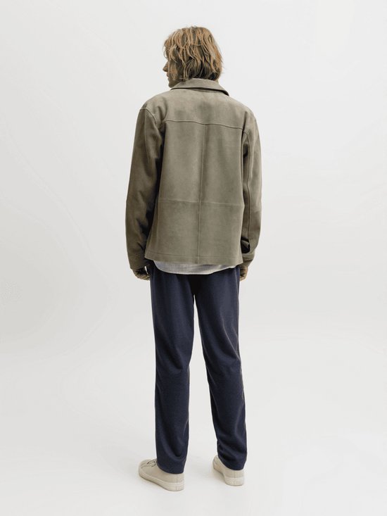 Achteraanzicht van het model in een olijfgroen suède jack, donkerblauwe chino's en beige sneakers.
