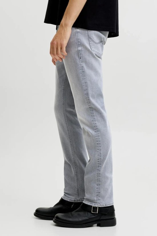Zij-aanzicht van een man in een grijze jeans met rechte pijpen en zwarte gesp laarzen.