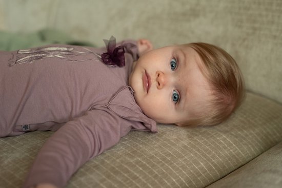 Baby met blauwe ogen in een oudroze shirt met strik en print van ballerina's.
