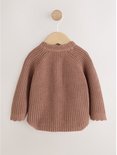 Een bruin gebreid babyvestje hangt aan een houten hanger.
