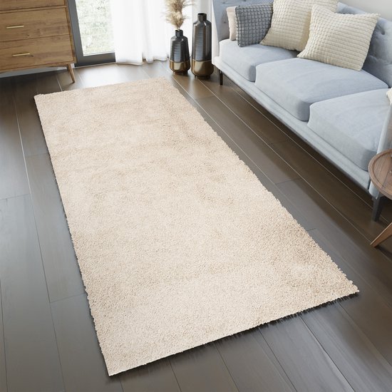 Un tapis de couloir crème à poils longs dans un salon, à côté d'un canapé gris.