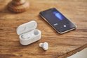 Witte oortelefoon en oplaadcase naast een smartphone.