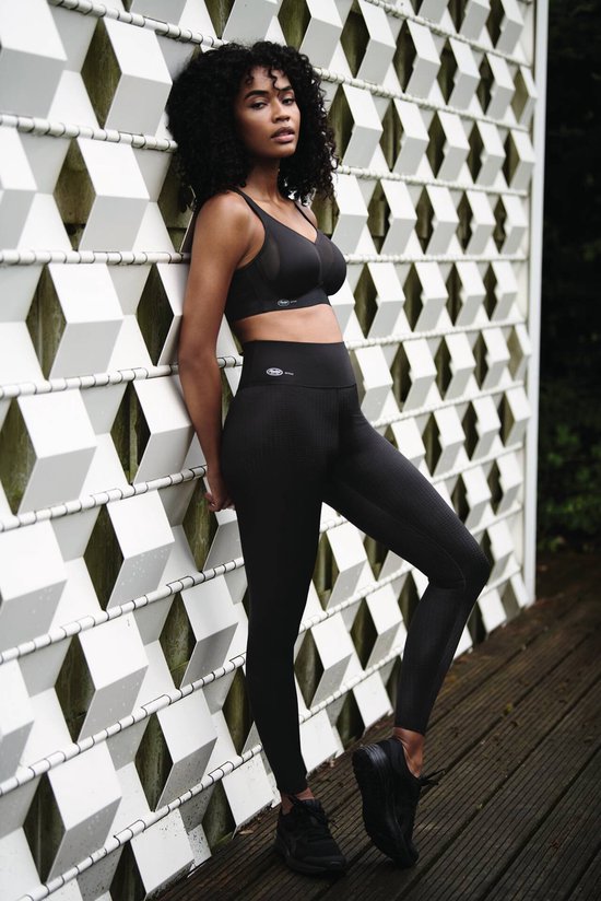 Model met een zwarte sportbeha en legging, staand bij een wit geometrisch raster.