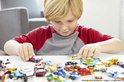 Jongen met sproeten speelt met een verzameling kleine auto's op tafel.