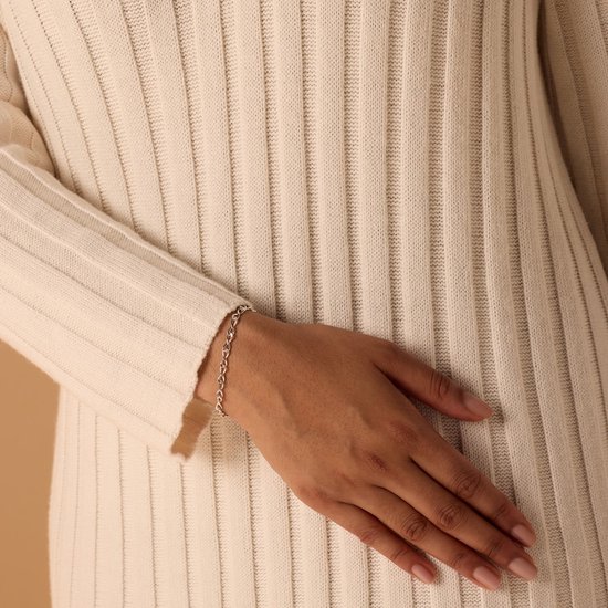 Close-up van een damesarm met een zilveren infinity schakelarmband om de pols.