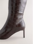 Detailopname van de hiel en de hak van de bruine knielaarzen met krokodillenmotief.