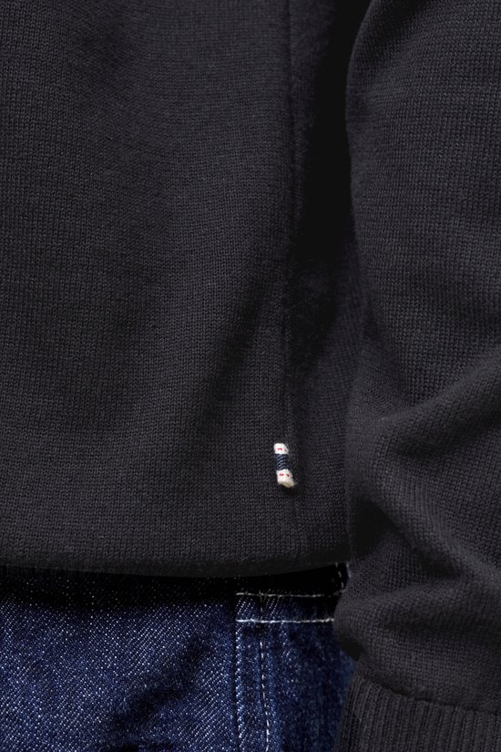 Detail van de onderkant van een zwart gebreid poloshirt met een klein labeltje met streepjes.