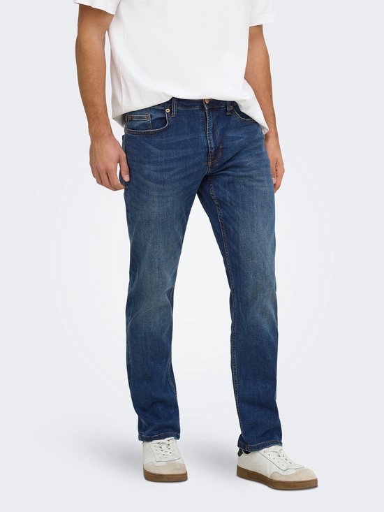 Model draagt een blauwe jeans met regular fit, gecombineerd met een wit T-shirt en wit-beige sneakers.