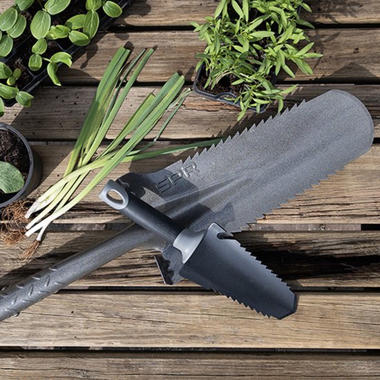 SPR spade en hand spade met gekartelde randen liggen op houten tafel naast plantjes en groen.