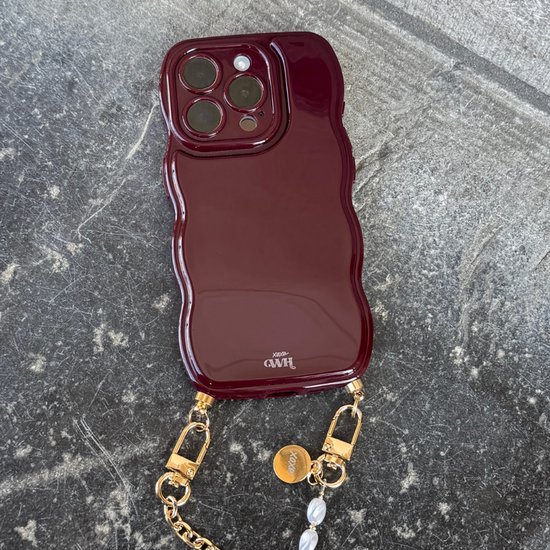 Glanzend bordeaux golvend telefoonhoesje met xoxo GWH-logo en gouden ketting met parels op een donkere ondergrond.