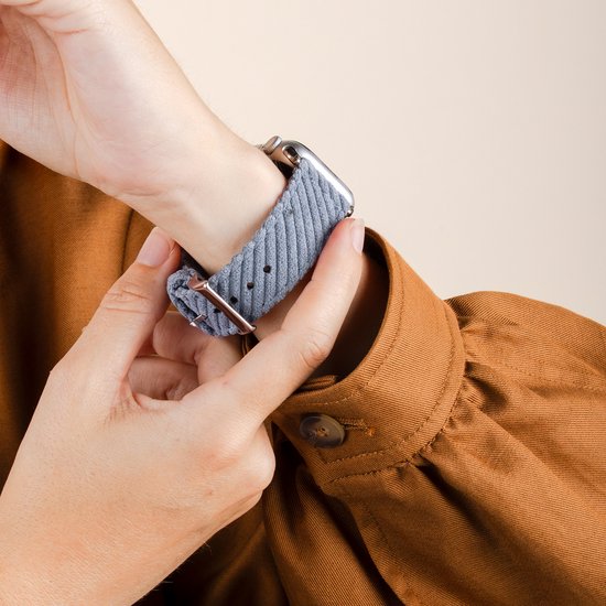 Vrouw bevestigt lichtblauw corduroy Apple Watch bandje met zilveren gesp.