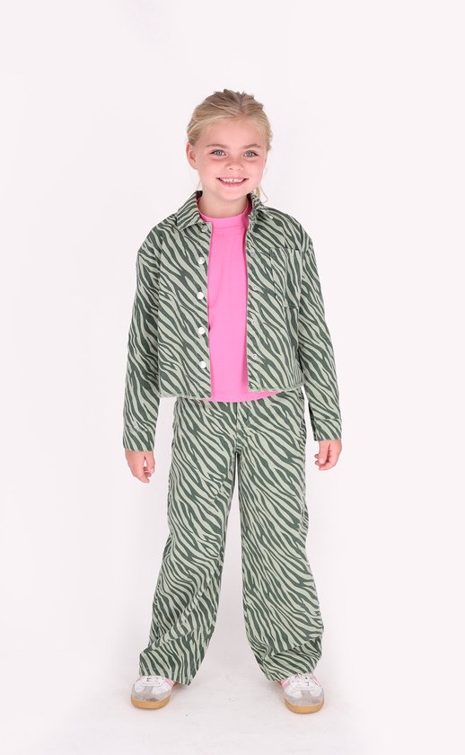 Een jong meisje met blond haar, lachend, in een groen met donkergroene zebraprint set.
