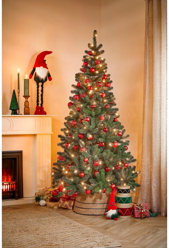 Kerstboom versierd met rode kerstballen, lampjes, een kerstman en cadeautjes bij de open haard.