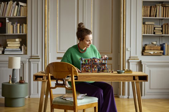 Een vrouw met een groene trui en rode ketting bouwt aan de LEGO Boekhandel.