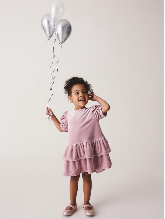 Meisje met zilveren ballonnen draagt een roze fluwelen jurk met pofmouwen en glinsterende stippen.