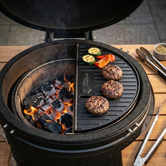 Grill Fanatics gietijzeren halve maan grillplaat met hamburgers en courgette boven houtskool op een kamado.