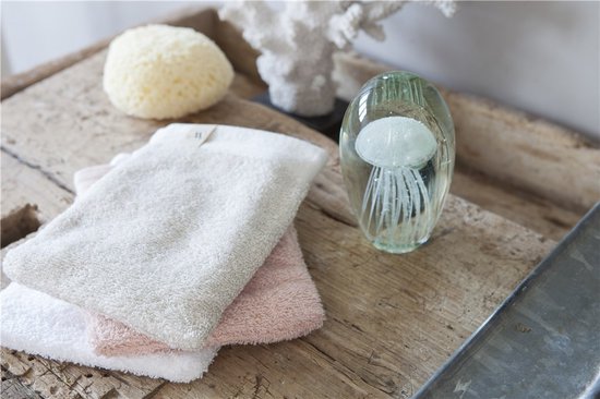 Gelaagde beige en roze washandjes op een houten ondergrond met een decoratieve glazen kwal.