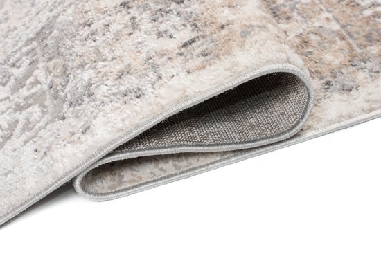 Gros plan détaillé du bord plié d'un tapis gris clair au motif délavé.