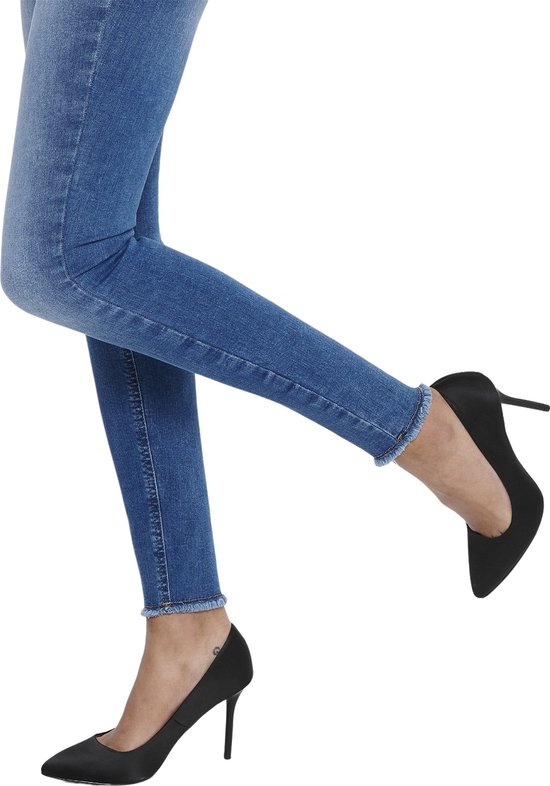 Blauwe skinny jeans met rafelige zoom, gedragen met zwarte pumps.