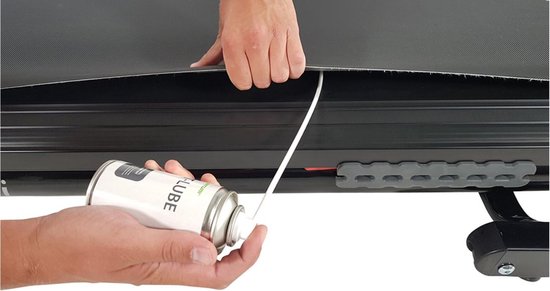 Handen gebruiken een spuitbus met T-LUBE om de onderkant van een loopband te smeren.