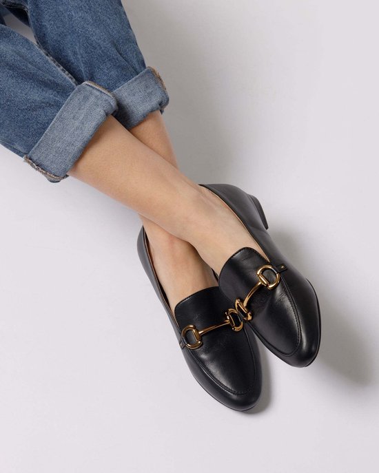 Zwarte leren loafers met gouden bitdecoratie, gedragen met een spijkerbroek met omgeslagen pijpen.