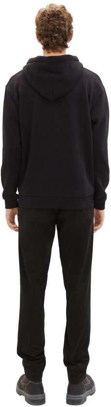 Man van achteren, draagt een zwarte hoodie, zwarte broek en grijze laarzen.