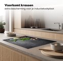 Zwarte inductie beschermer met betonprint, basilicum, rozemarijn, citroenpartjes, knoflook en peperkorrels, op een keukenblad met houten kasten.