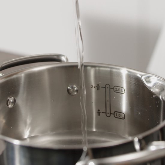 Water wordt in een roestvrijstalen pan gegoten met maataanduidingen.
