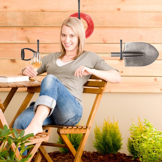 Vrolijke vrouw met glas witte wijn op een houten tuintafel, achtergrond met tuingereedschap.