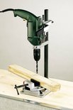 Groene boormachine op een boorstandaard met een werkstukklemming, een houten balk.