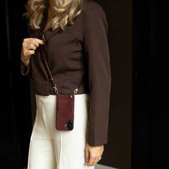 Vrouw met bruine blazer en witte broek, draagt een bordeauxrode croco backcover met een schouderband.
