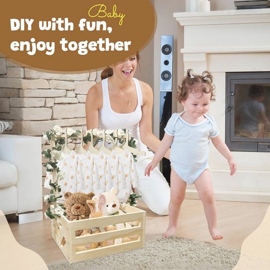 Baby met moeder bij houten babymand met kleding en knuffels, versierd met bloemen.