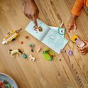 Un enfant et un adulte assemblent le set de chevaux LEGO Friends, avec voiture, remorque et chevaux sur une table.