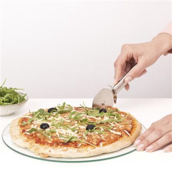 Main coupant une pizza avec un découpe-pizza en acier inoxydable. Pizza garnie de roquette et d'olives noires.