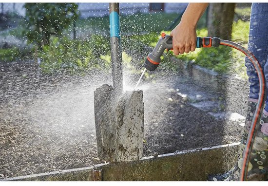 Hand sproeit een betonnen paal in een tuin met een Gardena spuitpistool.