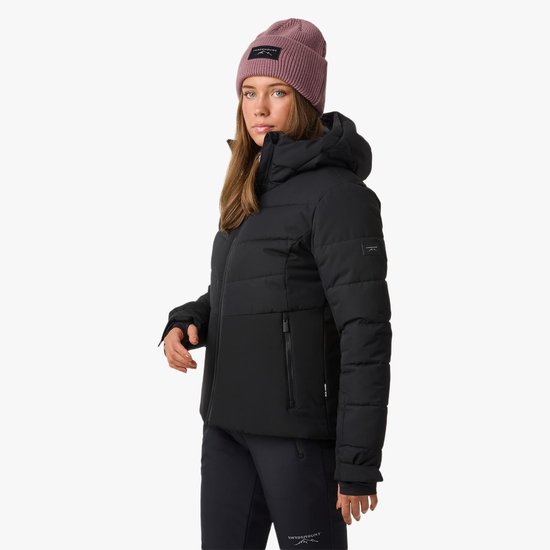 Model in zwarte ski-jas met capuchon, paarse muts en witte sjaal.