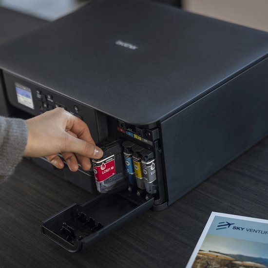 Close-up van een hand die een rode Brother inktcartridge in een zwarte printer plaatst.