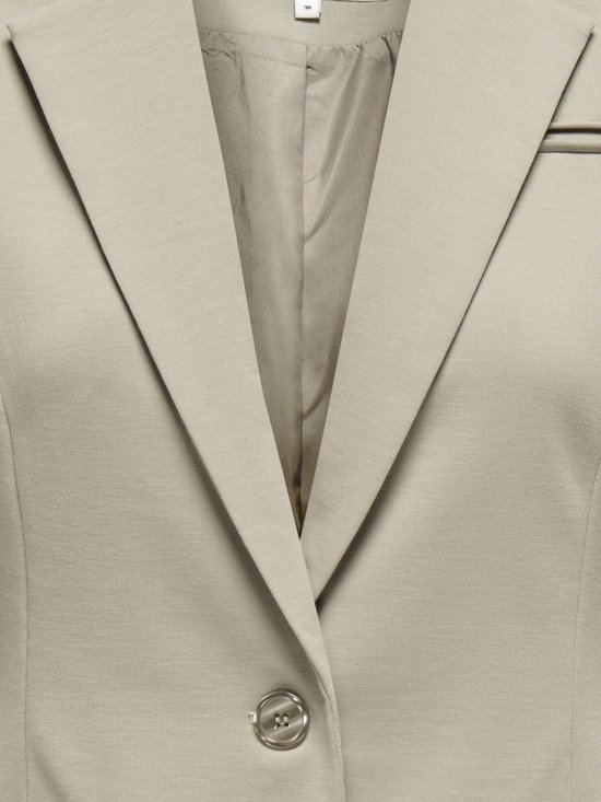 Close-up van de kraag en revers van een beige blazer, met een enkele knoopsluiting en een label.