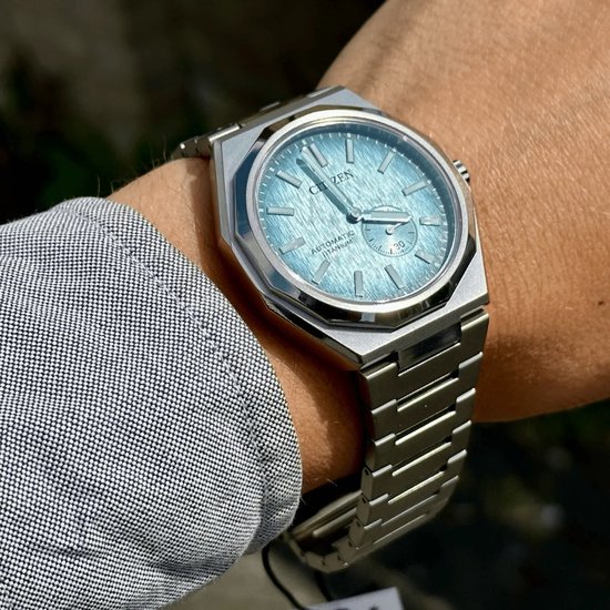 Citizen horloge gedragen op een arm, met zilverkleurige titanium kast en band. Lichtblauwe wijzerplaat met geborstelde textuur.