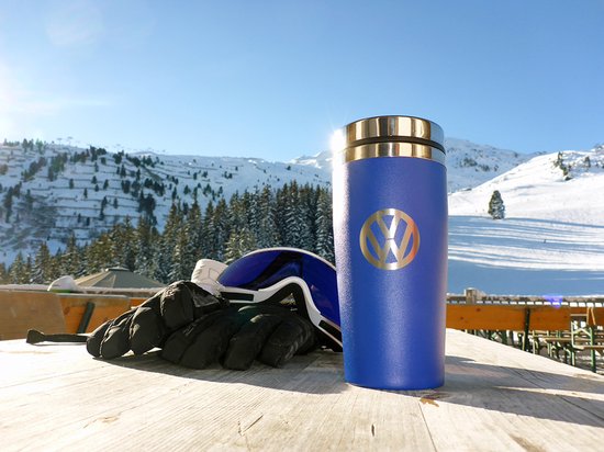 Korenblauwe thermosbeker met VW logo op een houten tafel in de sneeuw.