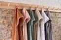 Zes badcapes in verschillende kleuren (bruin, roze, groen, beige, wit, grijs) hangen aan een houten rek.