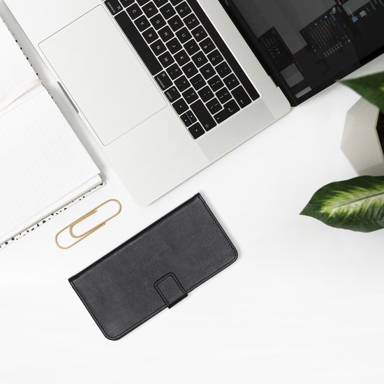 Zwarte lederen telefoonhoes op een bureau naast een laptop, notitieboekjes en een plant.