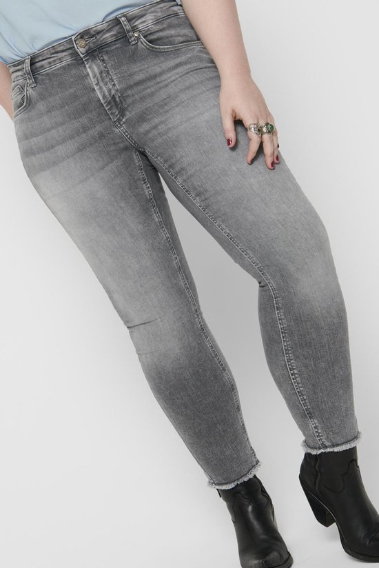Model in een lichtblauwe top en grijze skinny jeans met rafelige zoom, met zwarte laarsjes.