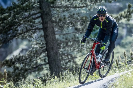 Man op racefiets in de bergen, draagt een zwart fietsjack met fluor gele details.