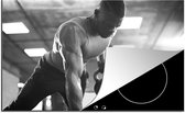 KitchenYeah® Inductie beschermer 81.2x52 cm - Een sterke man tilt tijdens fitness kettlebells omhoog - zwart wit - Kookplaataccessoires - Afdekplaat voor kookplaat - Inductiebeschermer - Inductiemat - Inductieplaat mat
