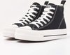 Paar zwarte hoge sneakers met witte veters, witte stiksels en dikke witte zolen.